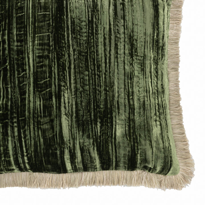 Green velvet pillow corner detail with beige fringe trim and vertical ribbed texture.