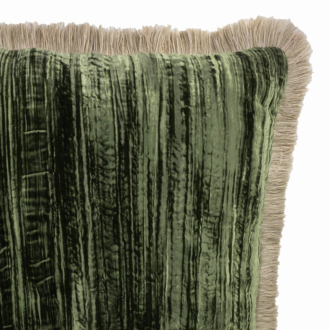 Close-up corner of green velvet pillow with beige fringe trim and textured sheen.