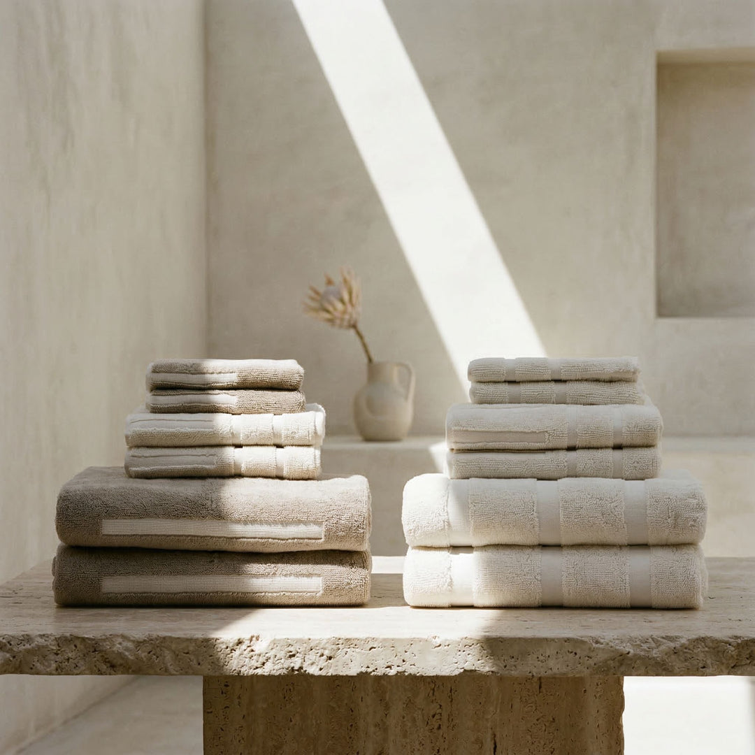 Stacked white and light gray cotton towels on a stone ledge.