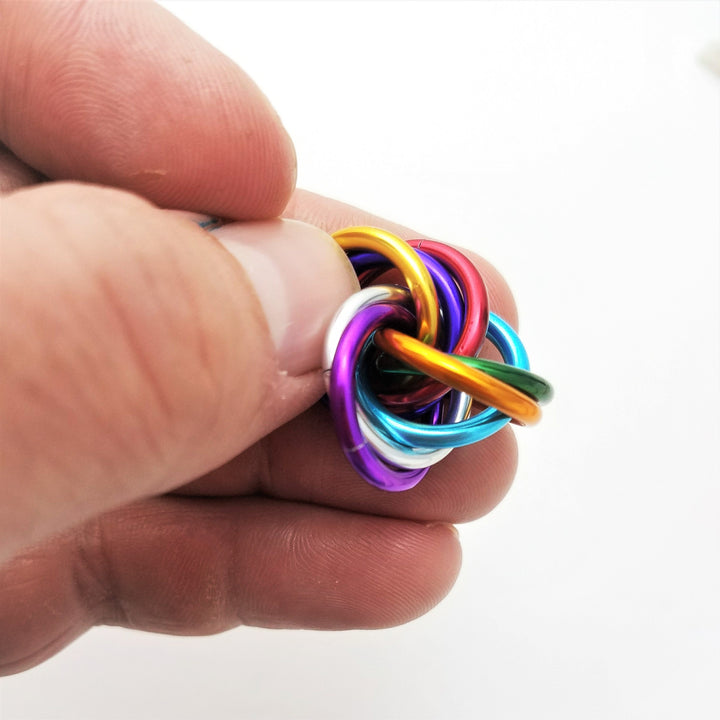 Multicolor metal fidget ball held in hand, braided loops in blue purple gold and pink