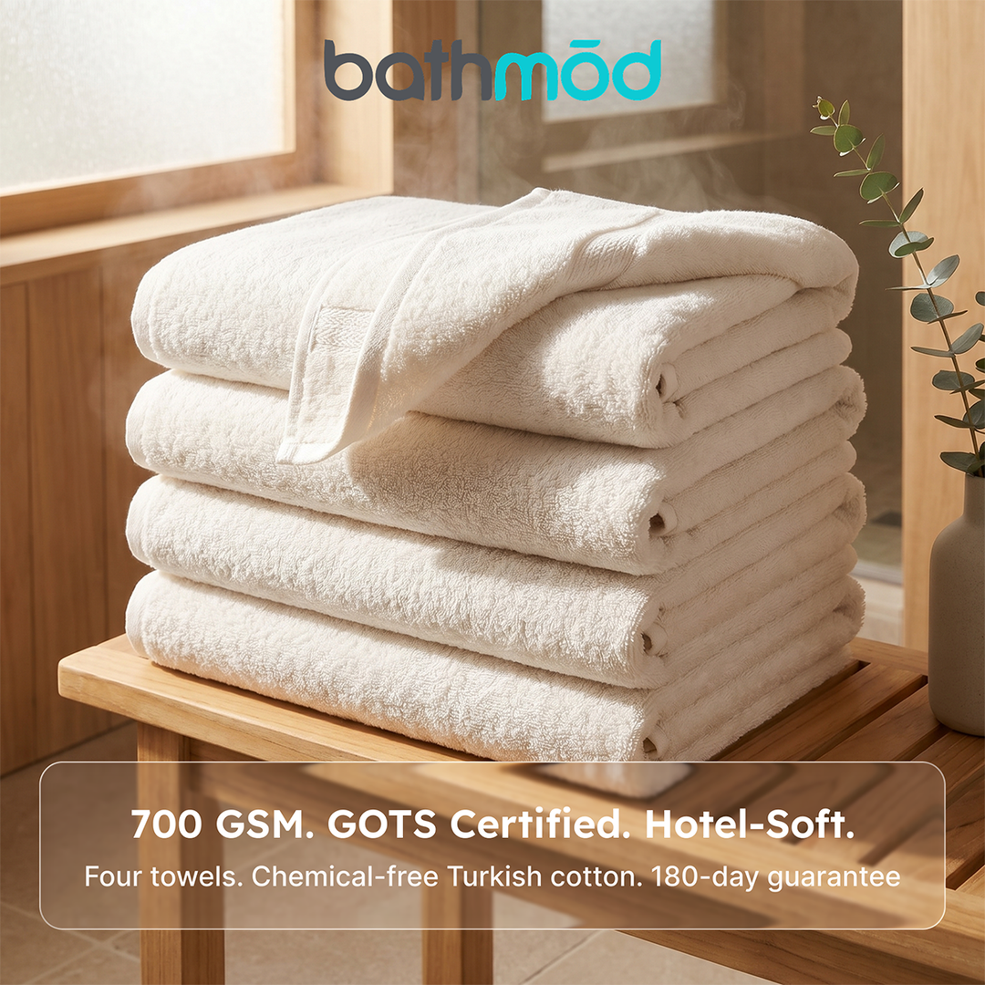 Stack of white bath towels, neatly folded in a four-towel set with stitched edges.