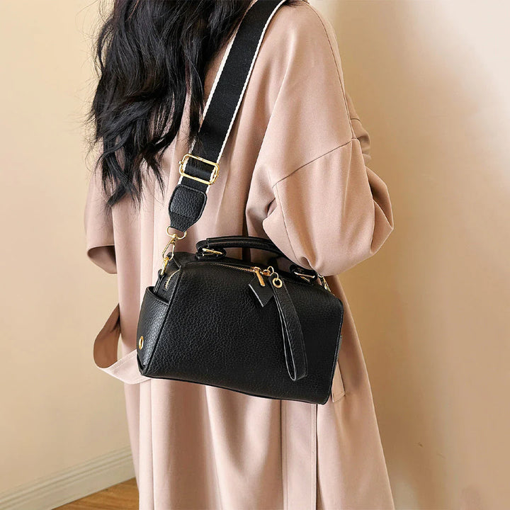Black mini barrel bag with crossbody strap and gold-tone hardware worn on model