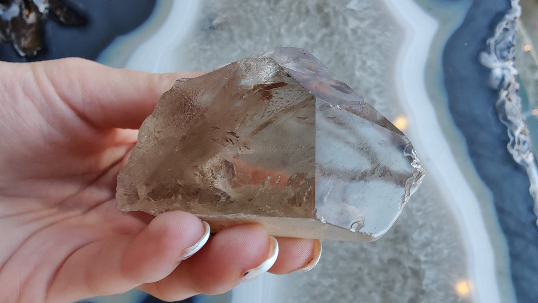 Smoky quartz crystal cluster fragment with smoky brown and clear facets, held in hand.