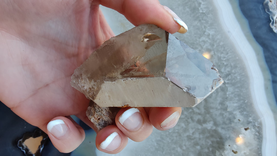 Smoky quartz crystal with sharp rectangular facets and smoky brown color, held in palm.