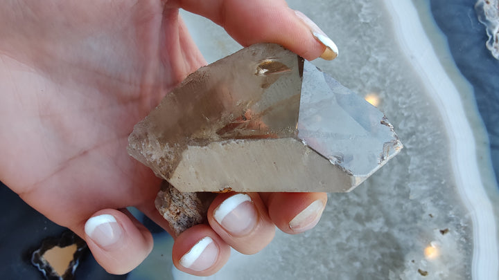 Smoky quartz crystal with sharp rectangular facets and smoky brown color, held in palm.