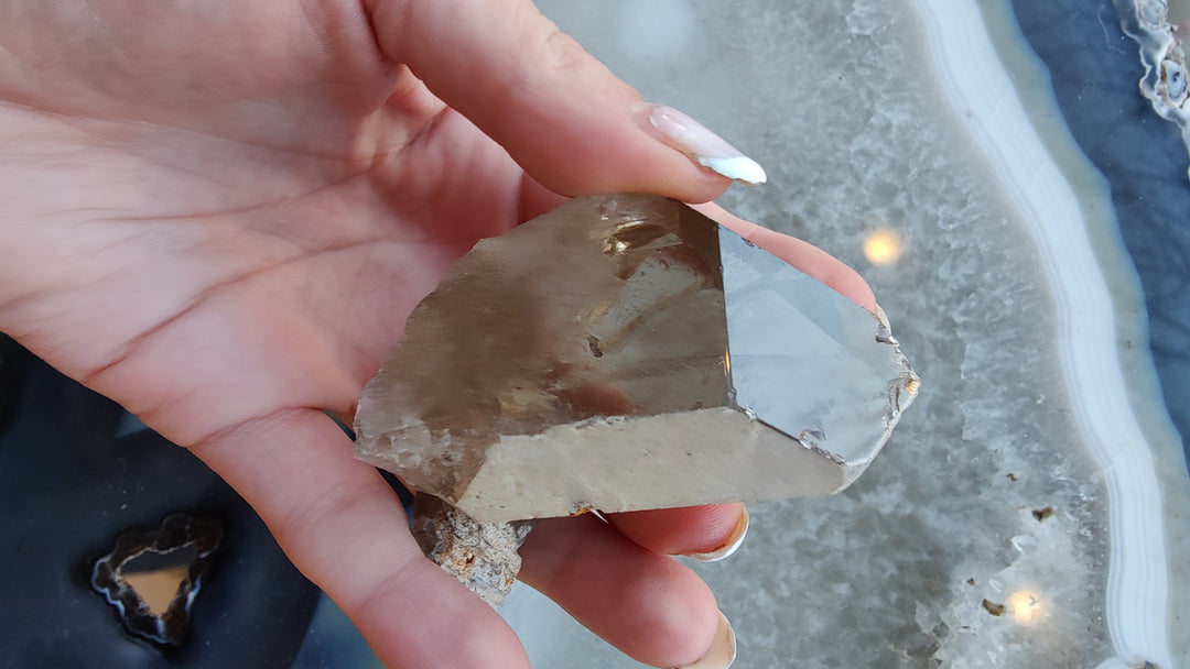Smoky quartz crystal with faceted surfaces and smoky brown shading, hand holding specimen.