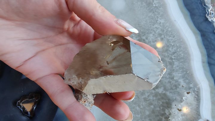 Smoky quartz crystal with faceted surfaces and smoky brown shading, hand holding specimen.