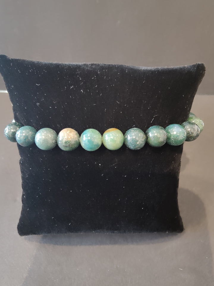 Beaded stone bracelet with green and cream round beads on a dark jewelry display