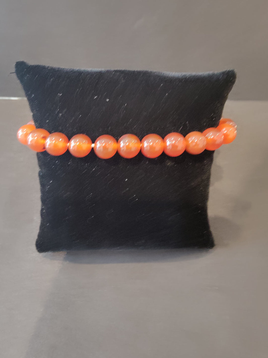 Beaded stone bracelet with orange round beads on a dark jewelry display