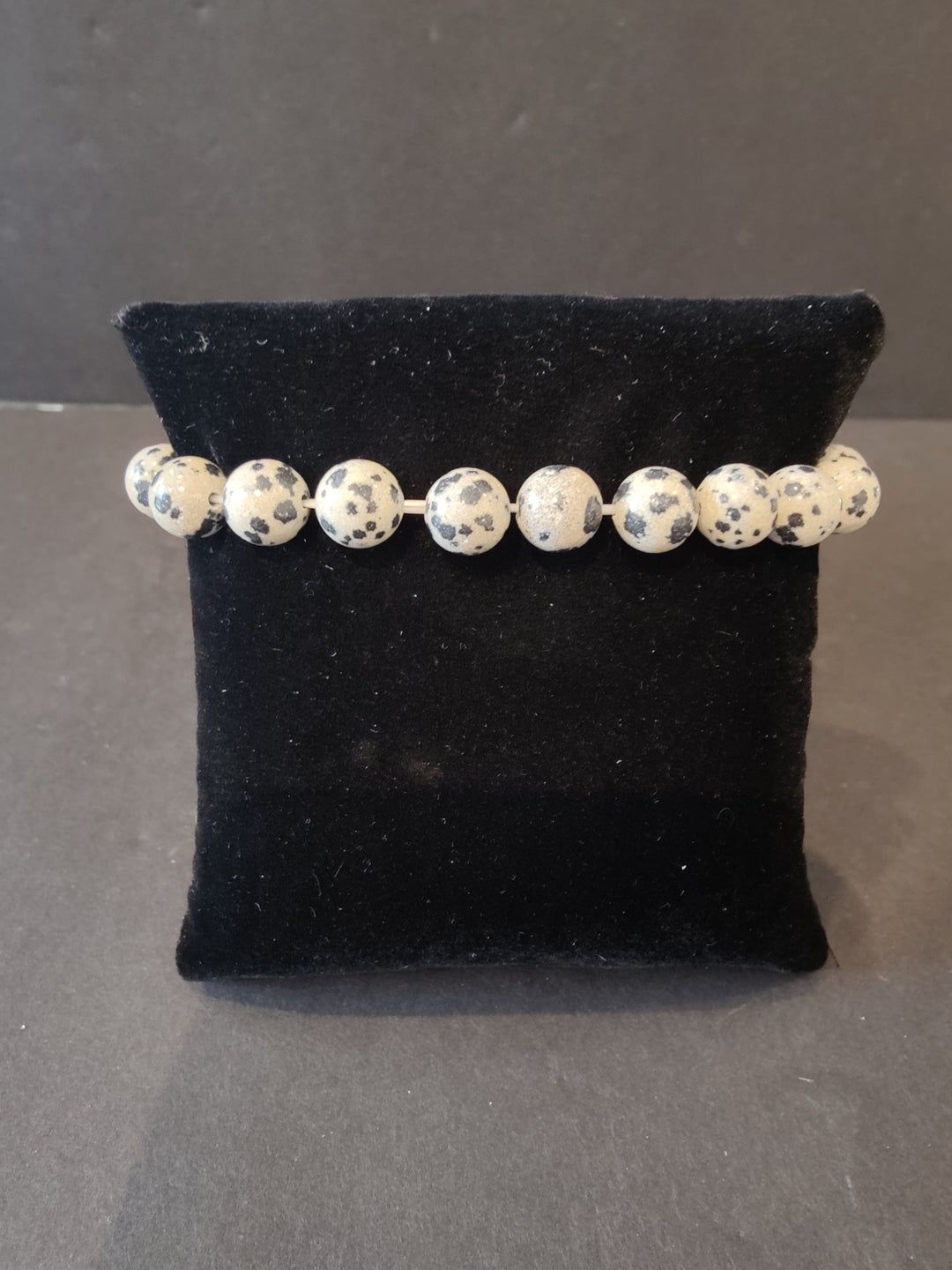 Beaded stone bracelet with speckled white and dark dot round beads on a dark display