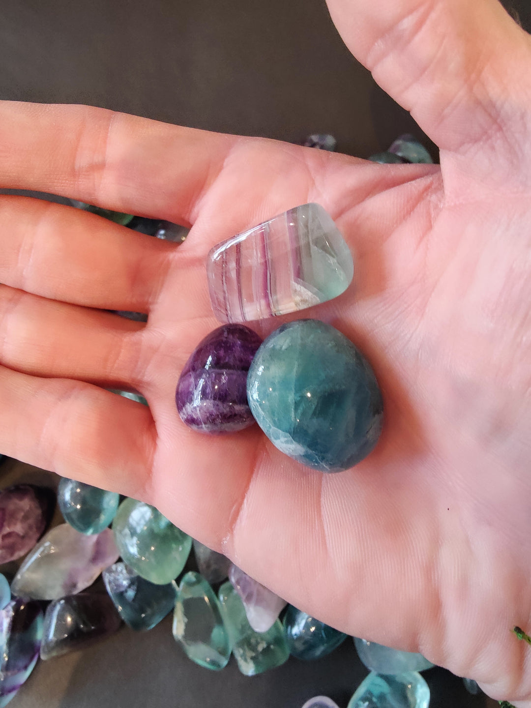 Two tumbled fluorite stones in hand: purple and teal oval pieces