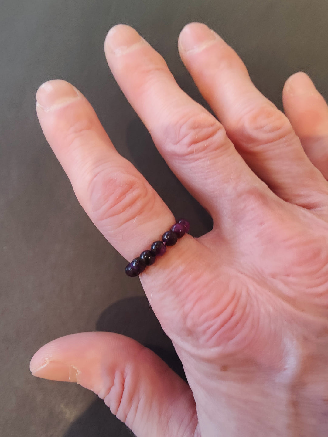 Beaded stone ring with dark purple 4mm beads on a hand.