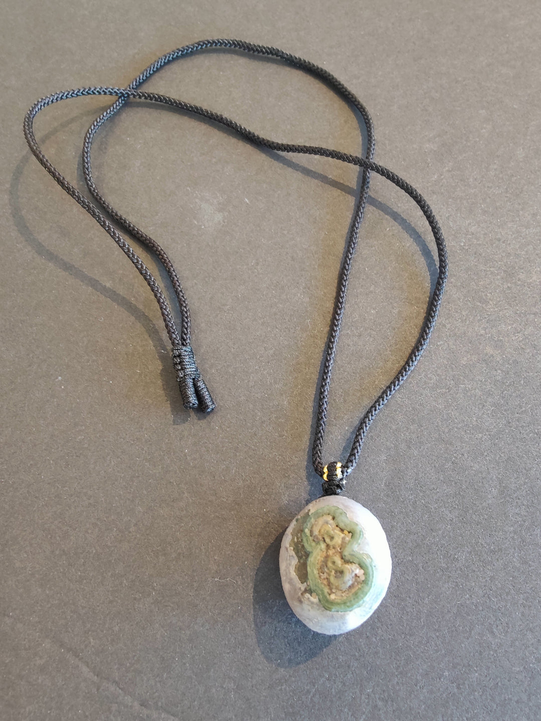 Eye agate pendant necklace with oval green-and-white stone on dark cord