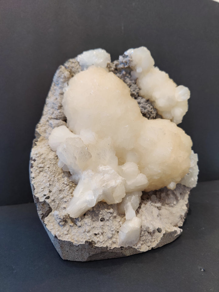 Heart-shaped rock specimen with cream crystal clusters over gray porous matrix