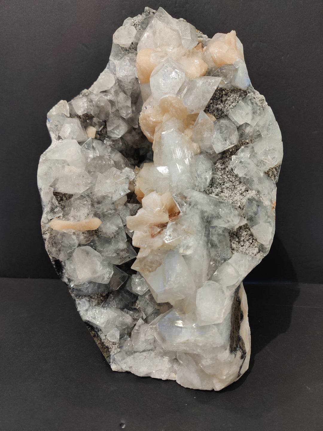 Mineral specimen with clear quartz and peach stilbite crystals on gray host rock