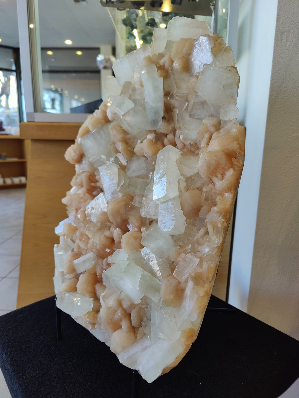 Tall clear and peach crystal cluster specimen on black stand