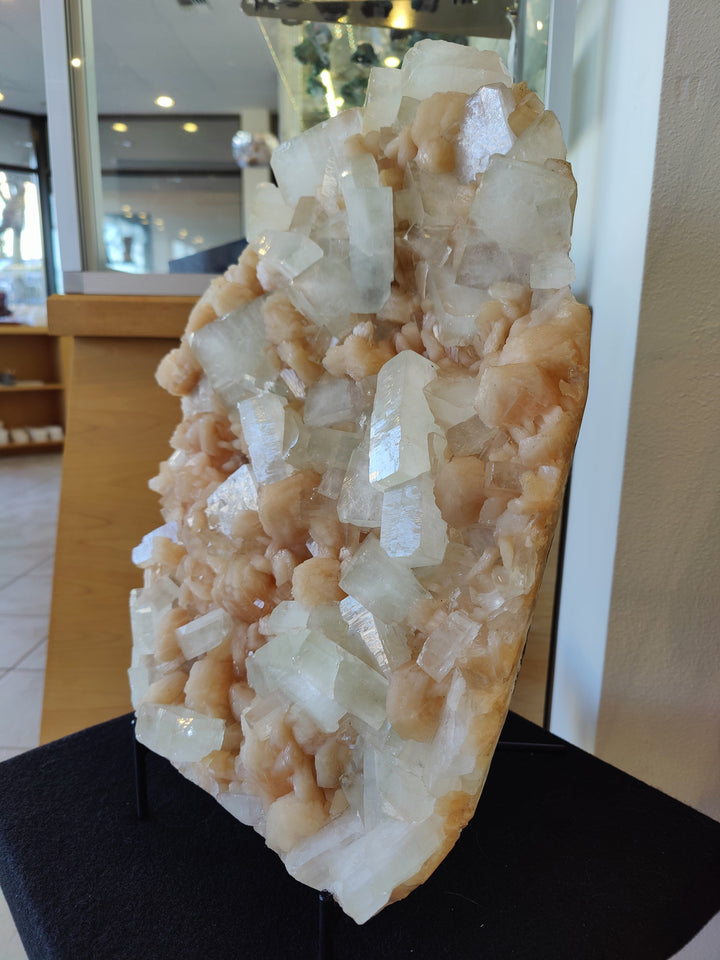 Tall clear and peach crystal cluster specimen on black stand