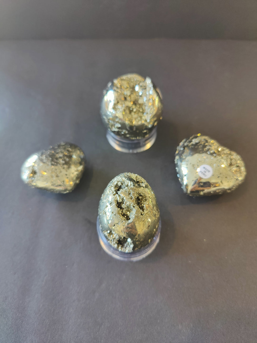 Polished pyrite stones—round sphere, egg, and heart shapes—in clear display domes