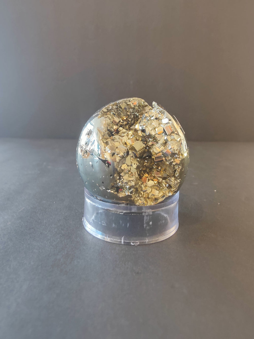 Polished pyrite gemstone dome with glittery gold surface, set in clear base
