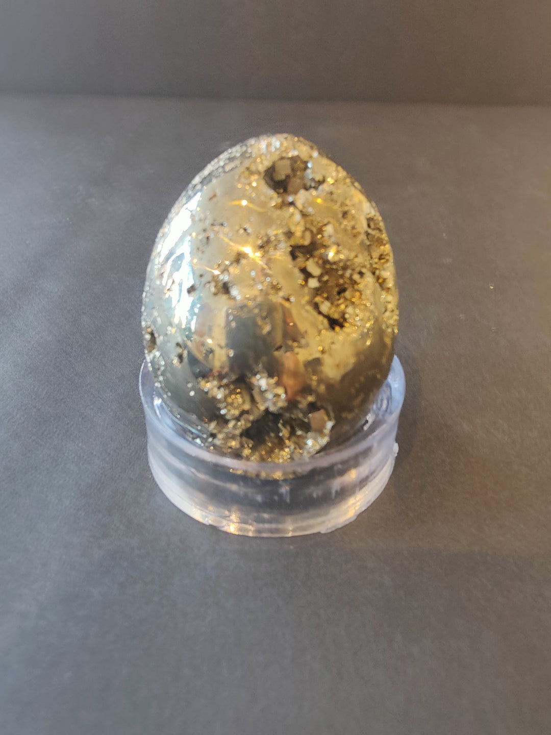 Polished pyrite egg-shaped gemstone with glittery gold flecks in a clear dome