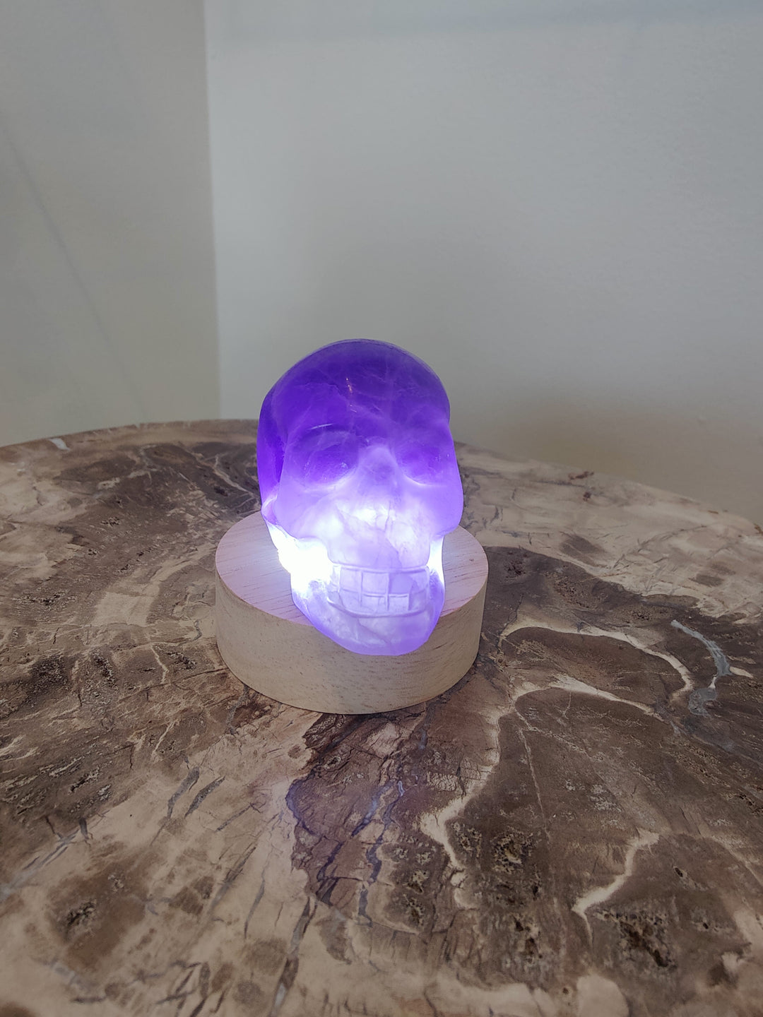 Purple fluorite skull sculpture on small round base, glowing purple light