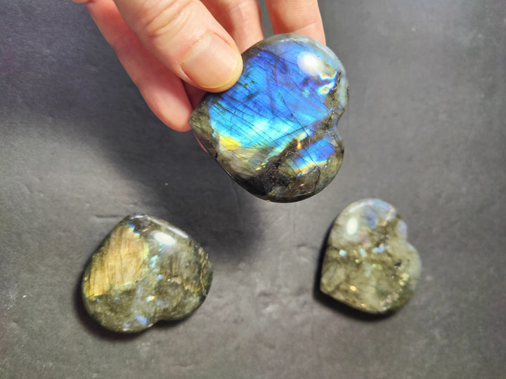 Polished labradorite heart gemstone in hand, blue sheen over golden green