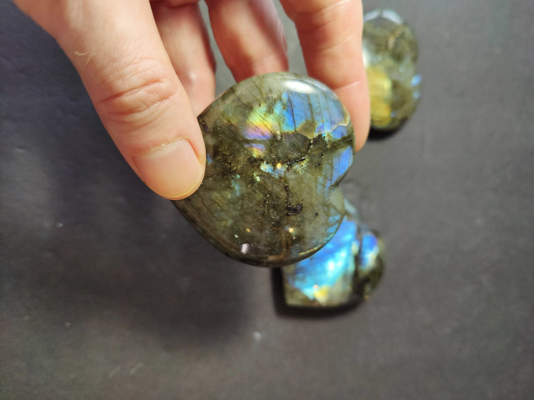 Hand holding a polished labradorite carved heart with dark green and blue highlights