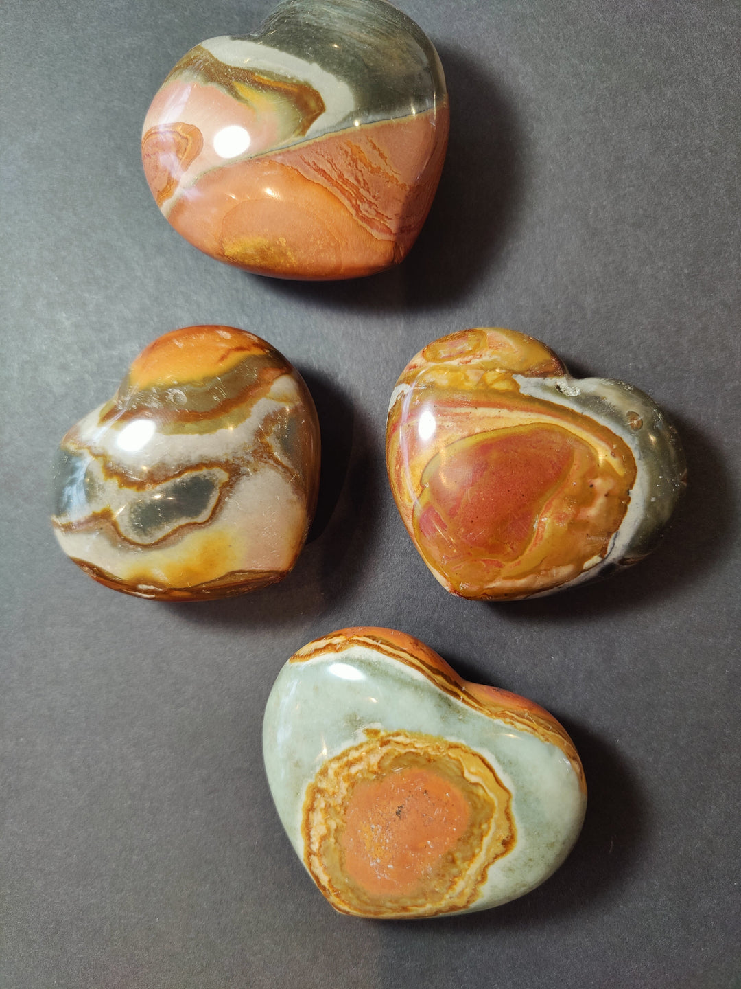 Polished polychrome jasper heart stones with carved swirls in orange, cream, and green
