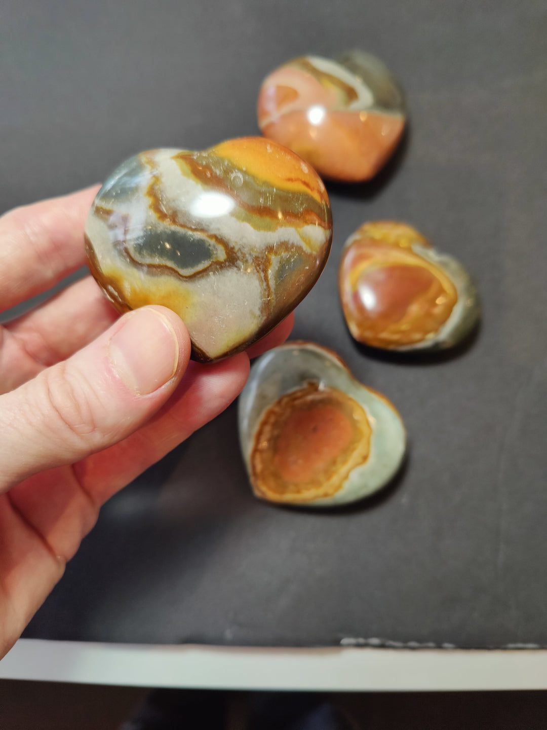 Carved jasper heart with glossy orange, cream, and gray banding, held in hand