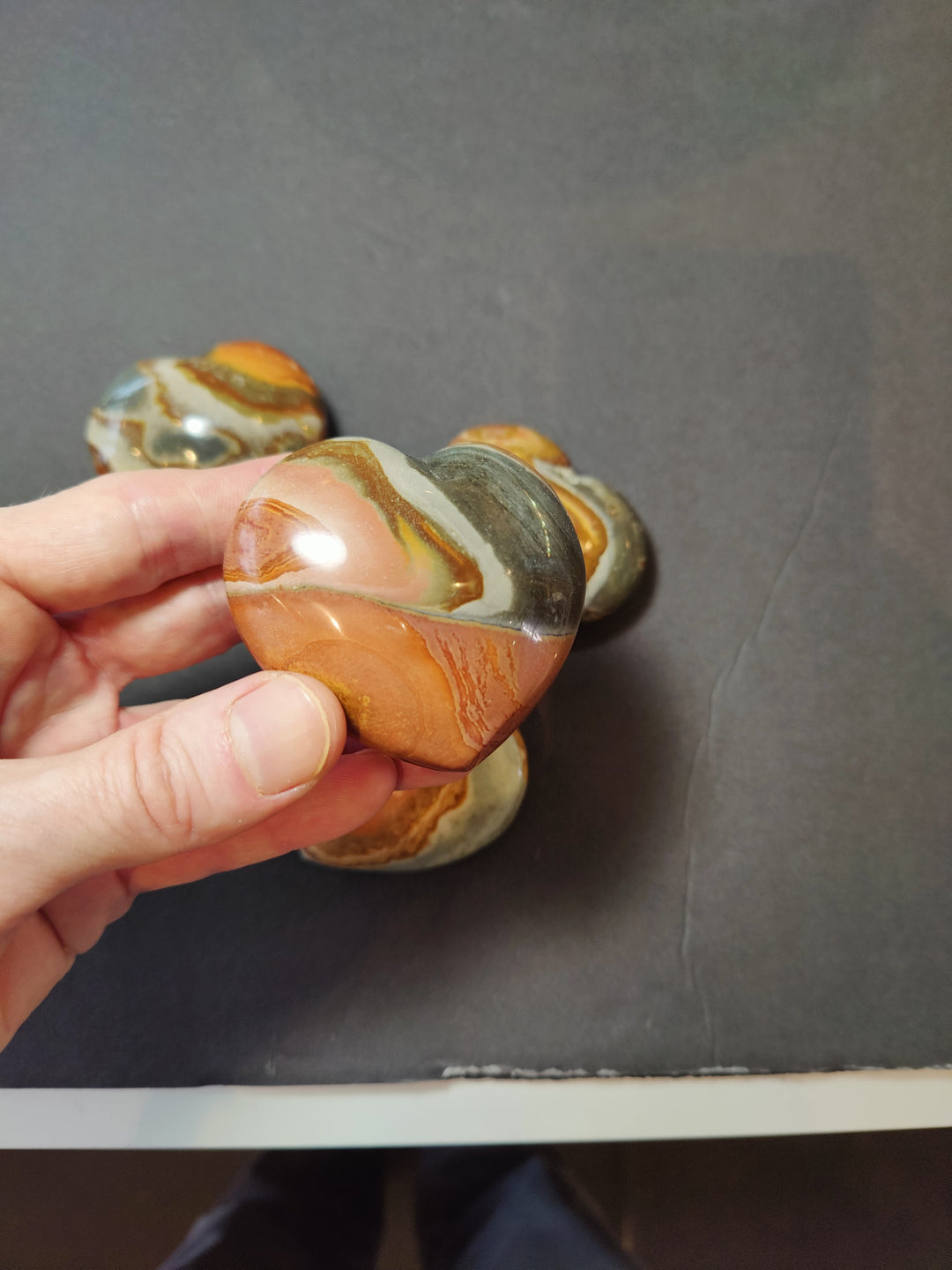 Polished jasper heart stone with orange, cream, and gray veining, viewed from side