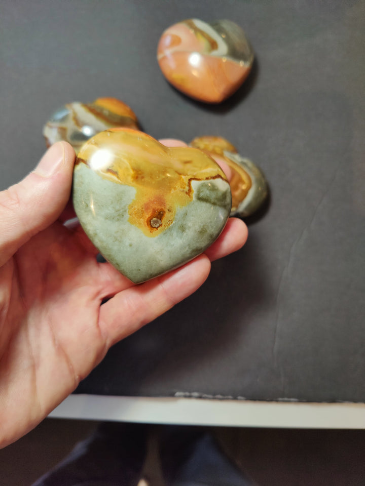 Carved jasper heart stone, glossy pale green with orange-brown veining, held up