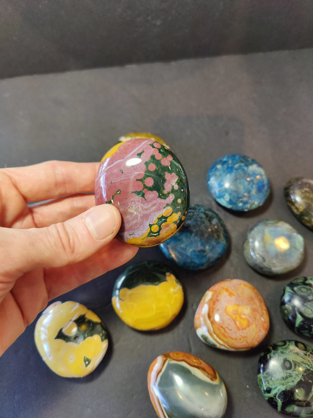 Polished pink palmstone with green floral speckles and yellow spots; rounded oval stone.
