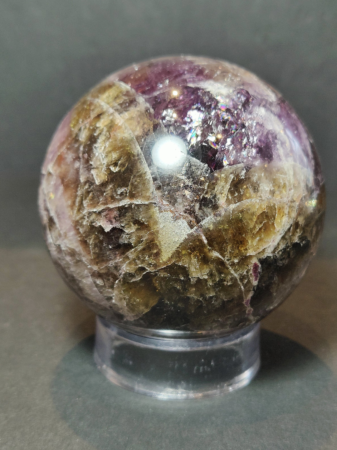 Polished amethyst purple crystal sphere with glittering flecks on clear metal stand