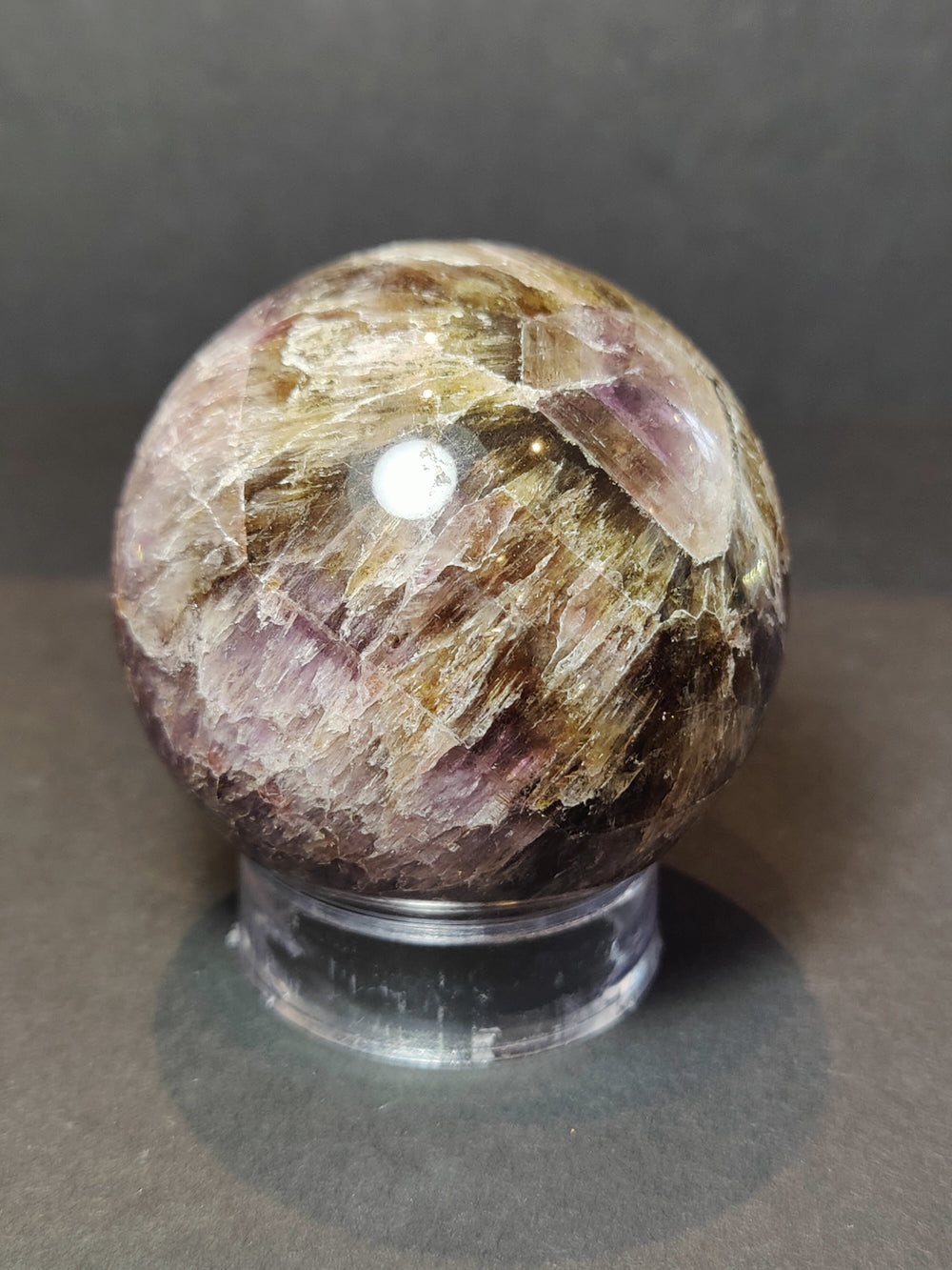 Polished purple and golden crystal sphere sculpture on black metal base