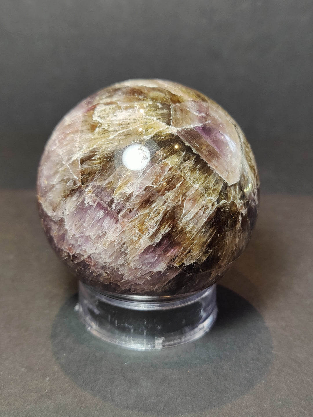Polished purple and golden crystal sphere sculpture on black metal base