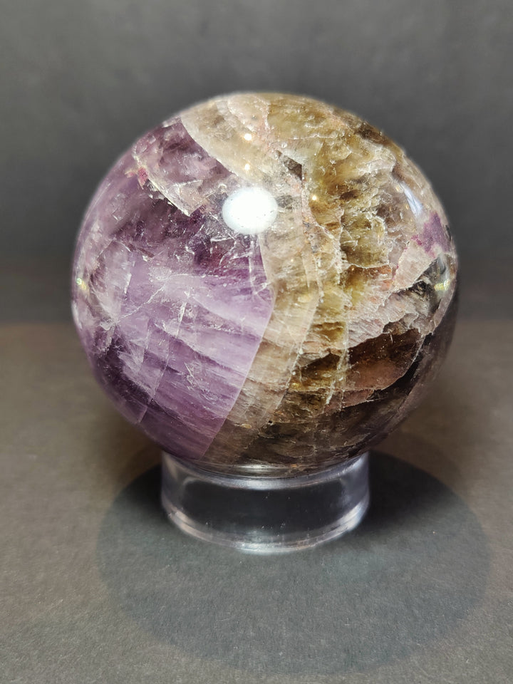 Polished amethyst purple crystal sphere with golden veins on metal base