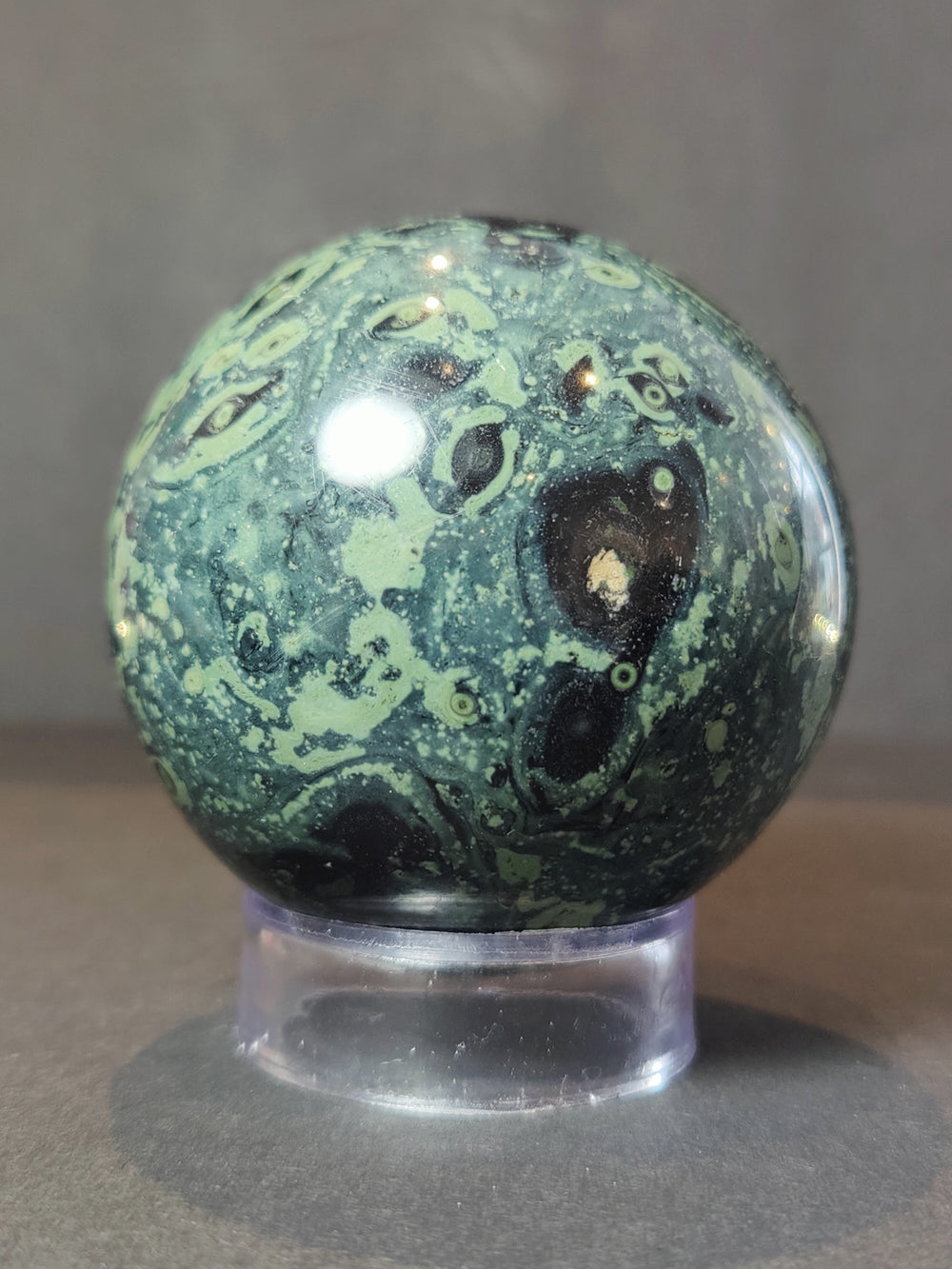 Polished green and black mottled jasper sphere on clear acrylic stand