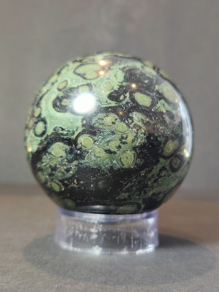Polished green and black jasper sphere with cloudy speckles on clear acrylic stand