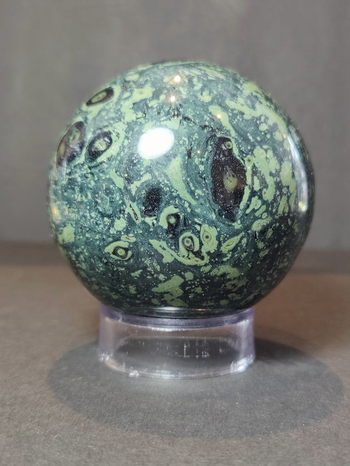 Polished green and black jasper sphere sculpture on clear acrylic stand