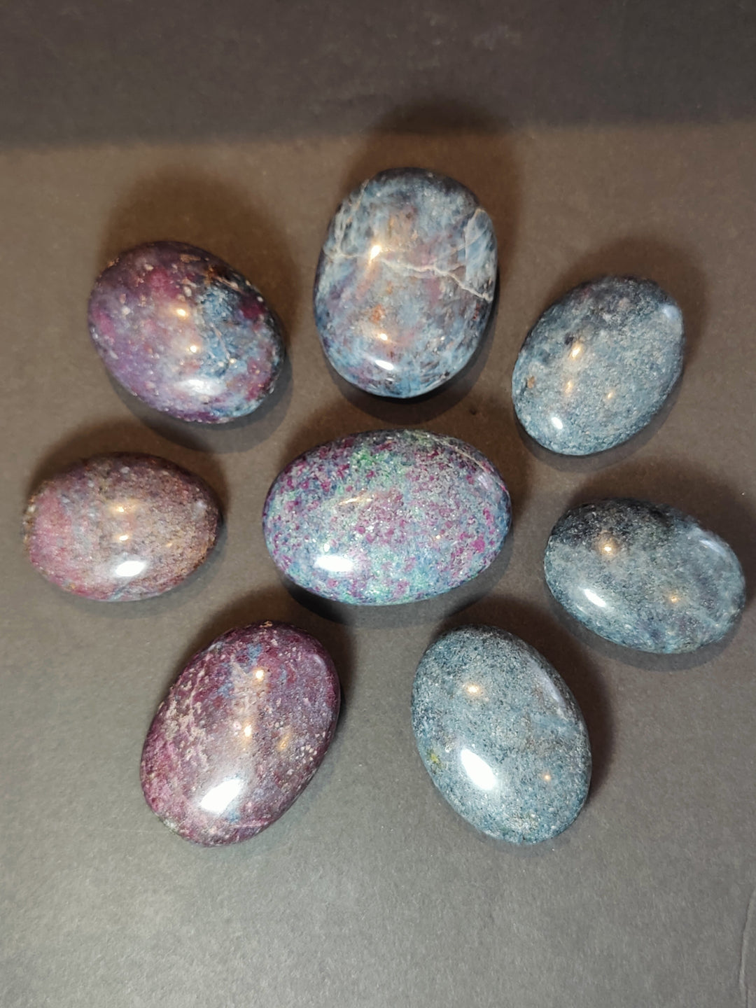 Polished ruby kyanite palmstones, smooth oval shapes with purple, blue, and teal speckling