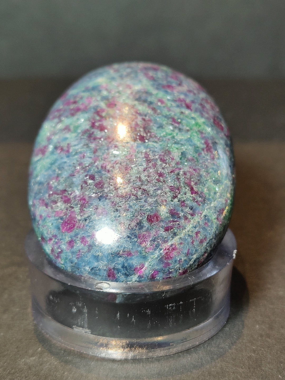 Polished ruby kyanite sphere on a black base, blue and pink glittery speckled stone