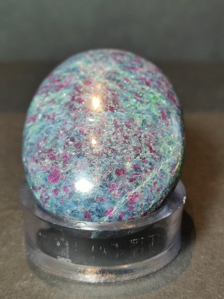 Polished ruby kyanite sphere on a black base, blue and pink glittery speckled stone