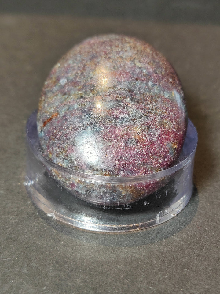 Polished ruby kyanite sphere on clear base, close-up pink, gold, and dark speckled pattern