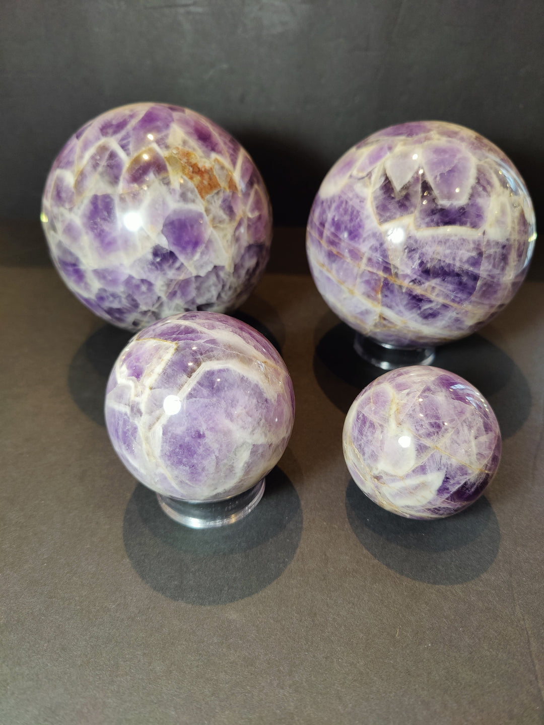 Polished amethyst sphere sculpture on clear base with purple-and-white pattern