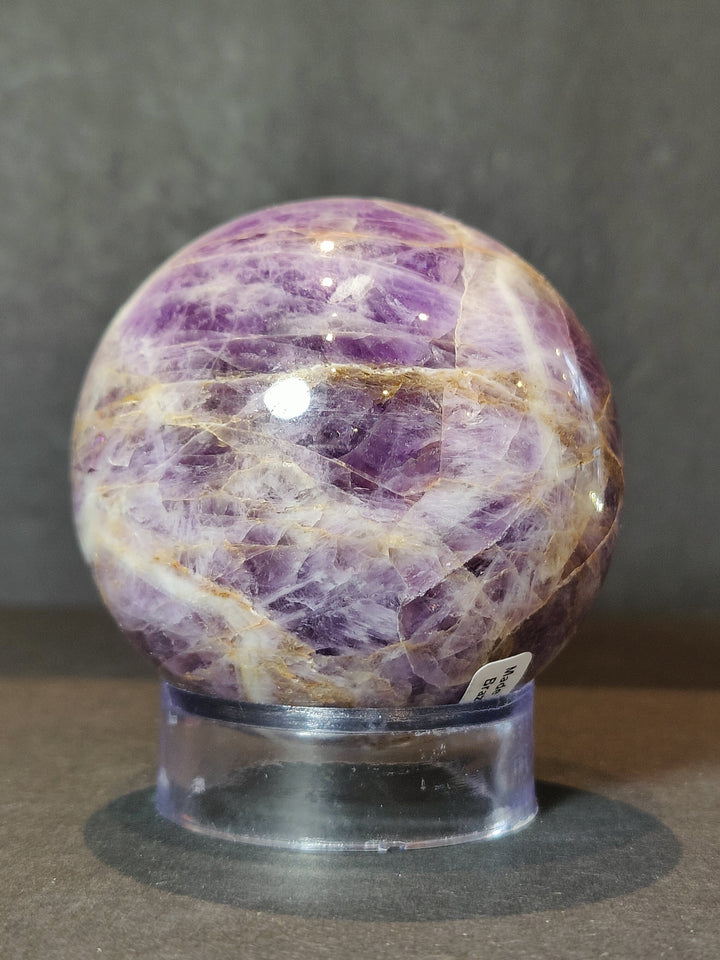 Polished amethyst sphere sculpture close-up on clear acrylic base, purple marbling