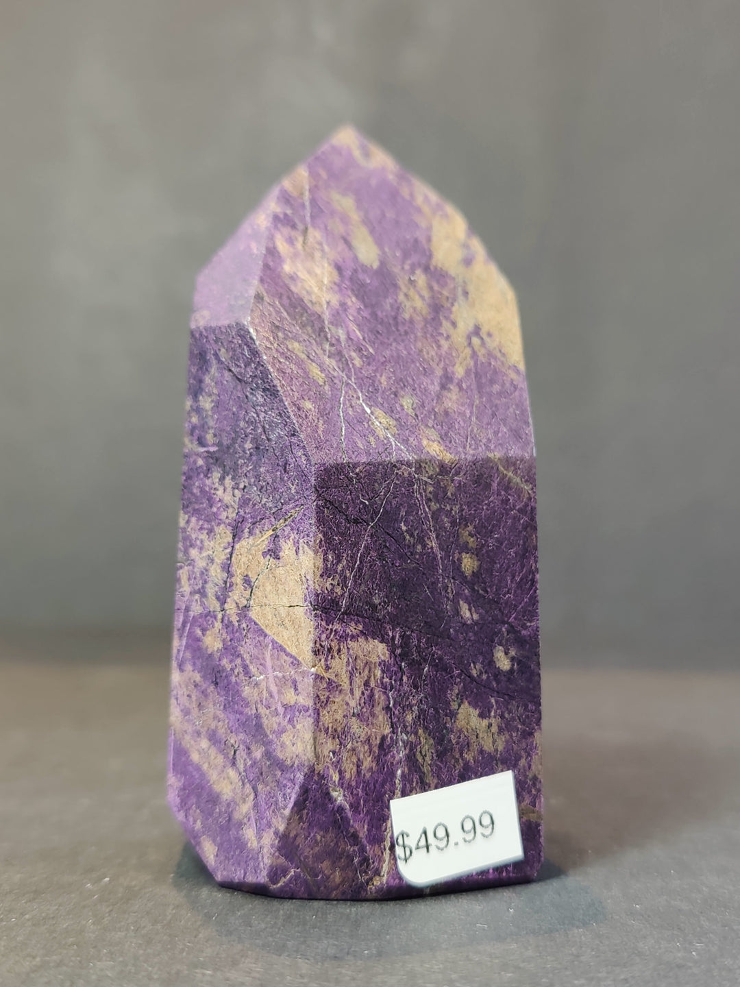 Polished purpurite obelisk tower sculpture with faceted purple face and dark banded base.