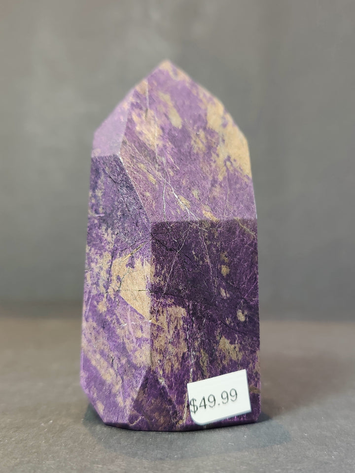 Polished purpurite obelisk tower sculpture with faceted purple face and dark banded base.