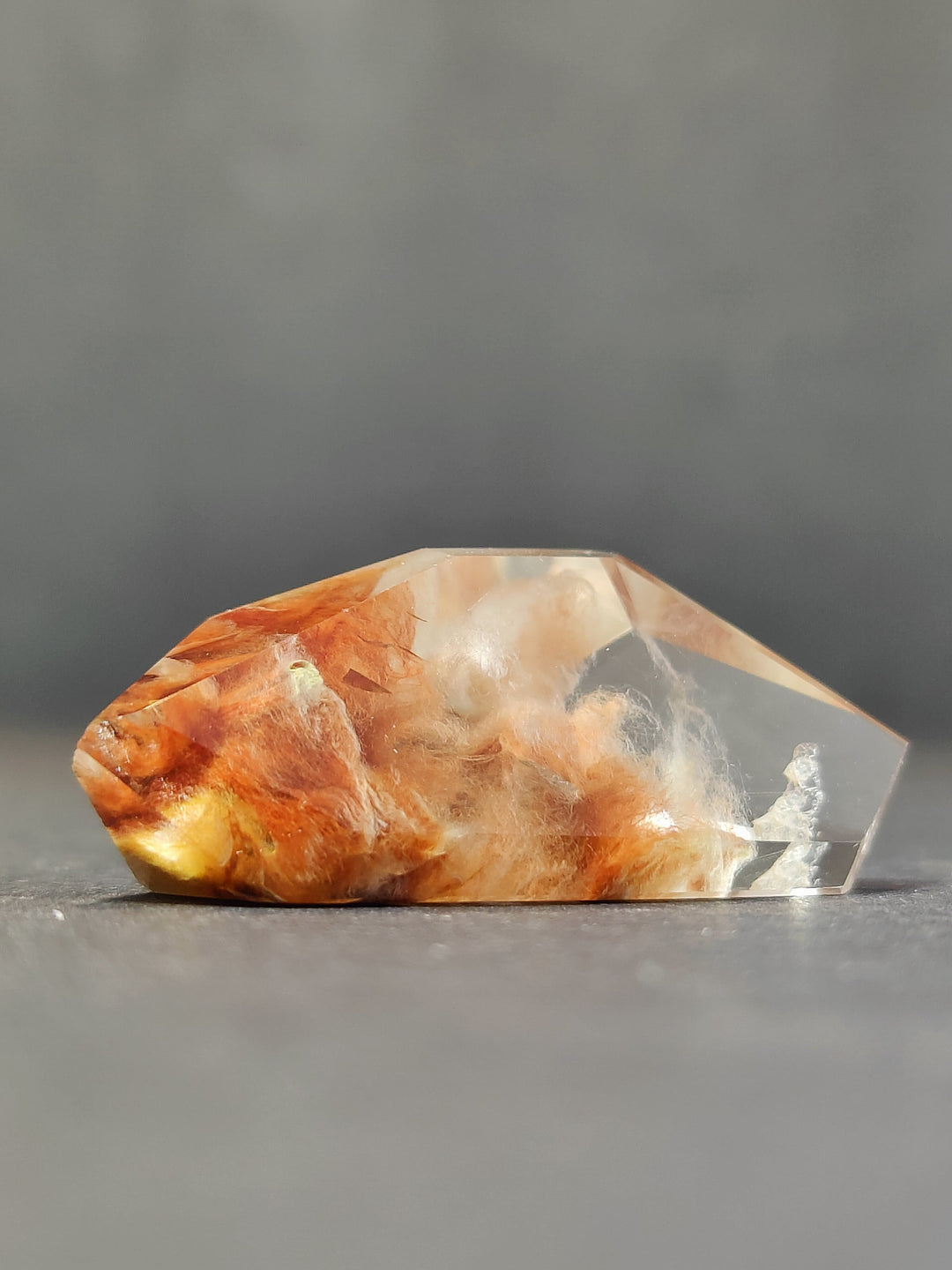 Polished freeform quartz crystal, orange and cream with clear faceted top.