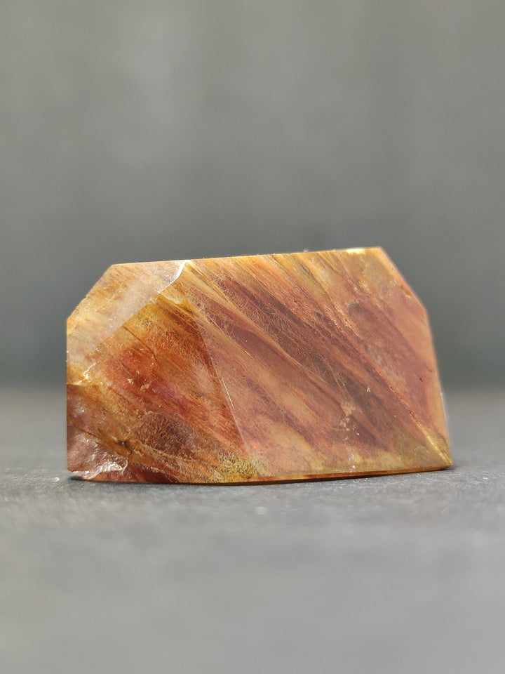 Polished freeform quartz crystal, flat rectangular face with orange and gold striations.
