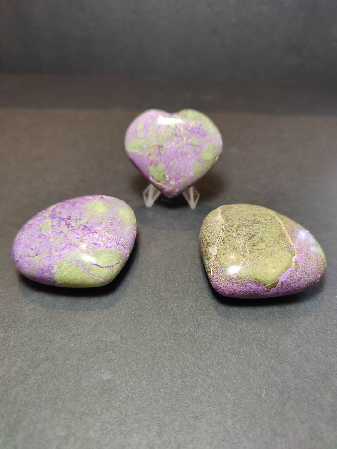 Polished gemstone heart and palmstone sculptures in purple and green on clear stands